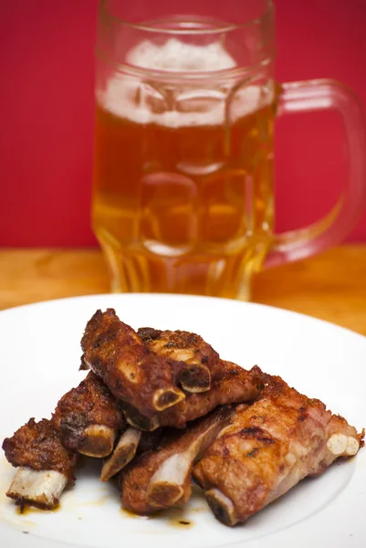 Costeletas de porco assadas em um prato branco com um jarro de cerveja ao lado — Fotografia de Stock