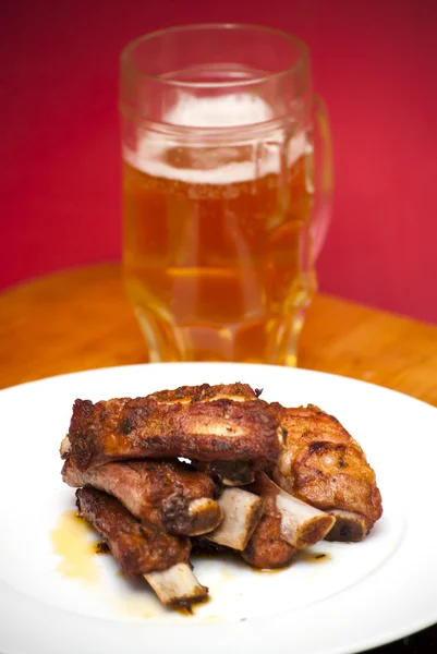 Côtes de porc rôties sur une assiette blanche avec un pichet de bière — Photo