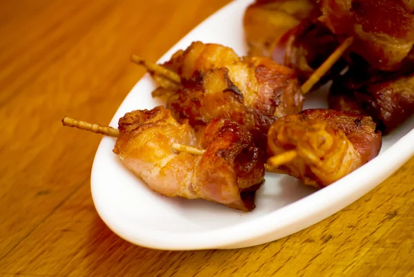 Rolls of slices of cooked bacon subject with a toothpick on a wh — Stock Photo, Image