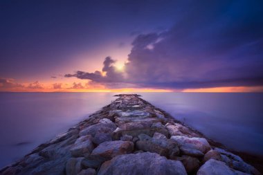 Gün batımında ufukta Rocky İskelesi ve Fırtına görünüyor. Uzun pozlama. Marina di Cecina Plajı, Toskana, İtalya.