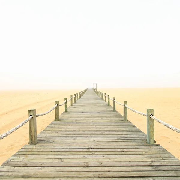Pasarela de madera sobre un fondo de playa de arena brumosa. Portugal . —  Fotos de Stock