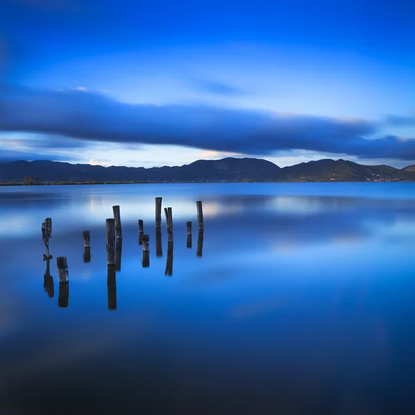 Molo o pontile di legno rimane su un lago blu tramonto e cielo refle — Foto Stock