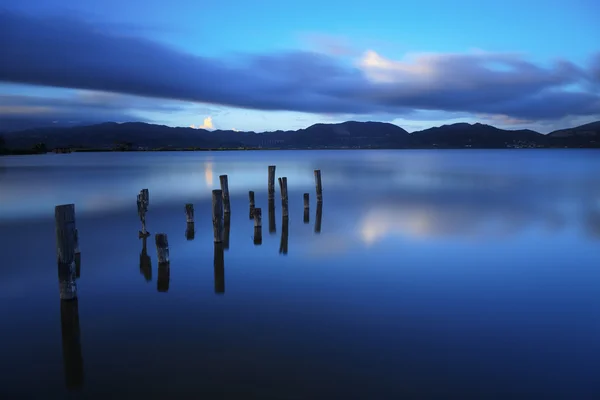 Muelle de madera o embarcadero permanece en un atardecer lago azul y refle cielo — Foto de Stock