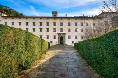 REGGELLO, TUSCANY - İTALYA 7 Aralık 2025 Vallombrosa Manastırı Cephesi. Yeşil çitlerden geçen taş bir patika manastır girişine çıkıyor.