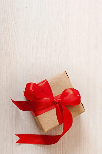 Ahşap bir arka planda kırmızı kurdeleli hediye kutusu. — Stok fotoğraf