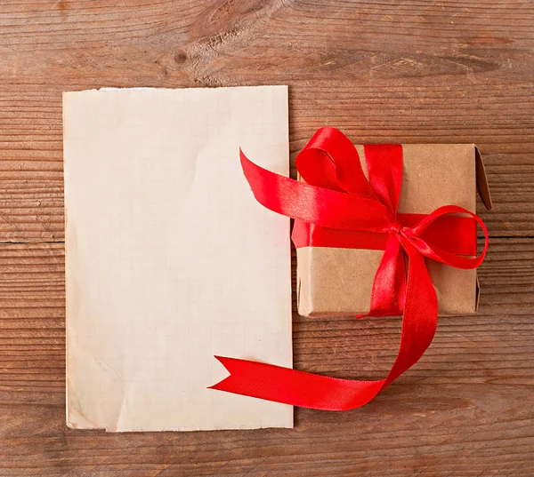 Подарок и лист бумаги на старом деревянном фоне — стоковое фото