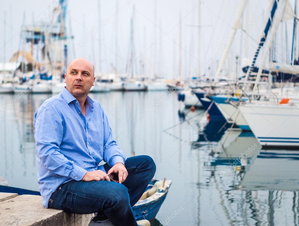Businessman sitting by expensive sailing boats and yachts in a c