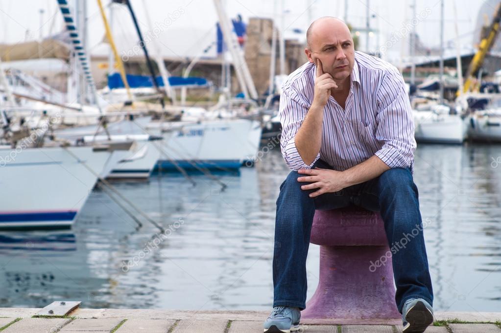 Businessman sitting by expensive sailing boats and yachts in a c
