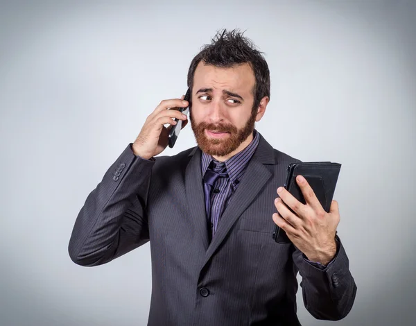 Geschäftsmann spricht auf seinem Smartphone und schaut verdutzt in die Kamera — Stockfoto