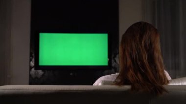 Kız, karanlık bir odada yeşil ekranlı televizyon izliyor..