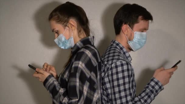 マスクの男と女が一緒に立ってスマートフォンを使う — ストック動画