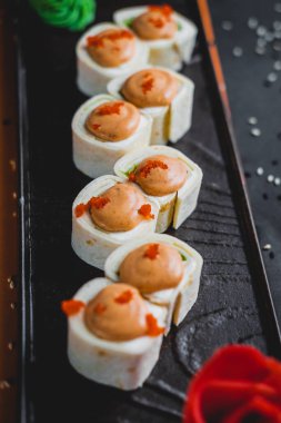 Somon ve yılan balıklı rulo siyah bir tabakta güzel bir sunumla