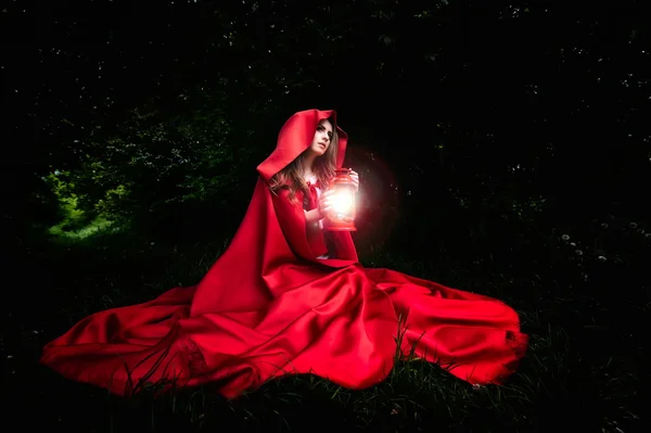 Gyönyörű nő piros köpenyt, és a lámpa az erdőben — Stock Fotó