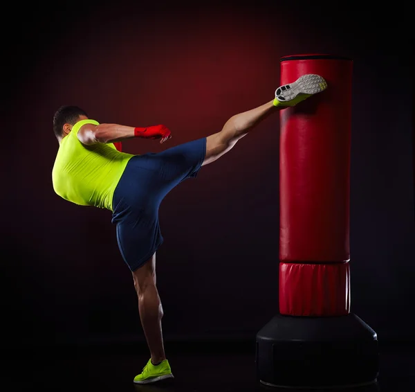 Joven hombre ejercitando bolsa de boxeo en estudio — Foto de Stock