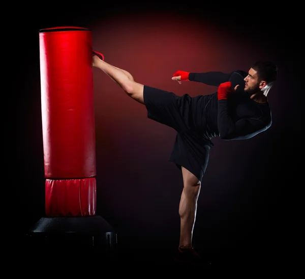 Jovem homem exercitando saco de boxe no estúdio — Fotografia de Stock