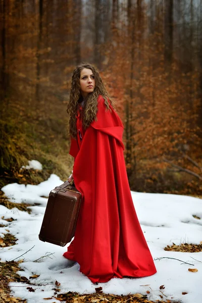 Schöne Frau mit rotem Mantel und Koffer allein im Wald — Stockfoto