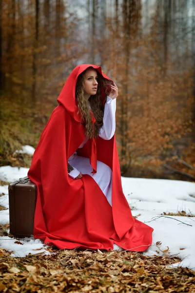 Schöne Frau mit rotem Mantel und Koffer allein im Wald — Stockfoto