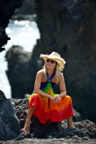 Young beautiful woman between black rocks on the beach in summer — Stock Photo, Image