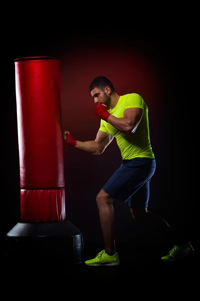 Jovem homem de pé exercitando com saco de boxe no estúdio — Fotografia de Stock