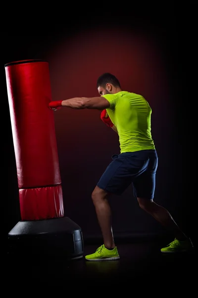 Young man standing exercising with  boxing bag in studio — Stock Photo, Image
