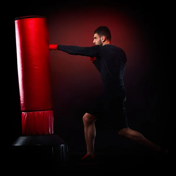 Joven hombre ejercitando bolsa de boxeo en estudio — Foto de Stock