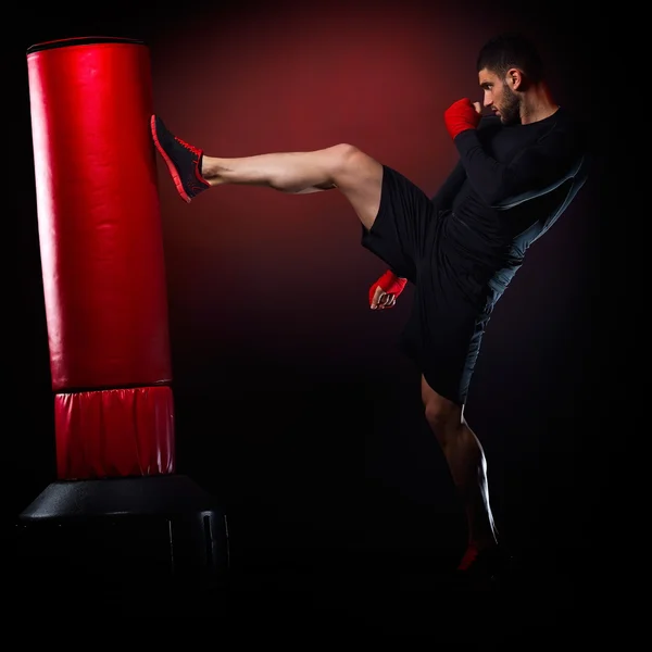 Joven hombre ejercitando bolsa de boxeo en estudio — Foto de Stock