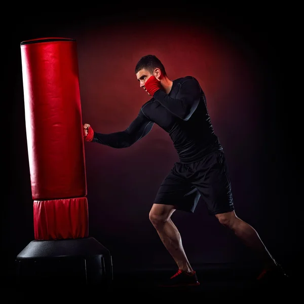 Jovem homem exercitando saco de boxe no estúdio — Fotografia de Stock