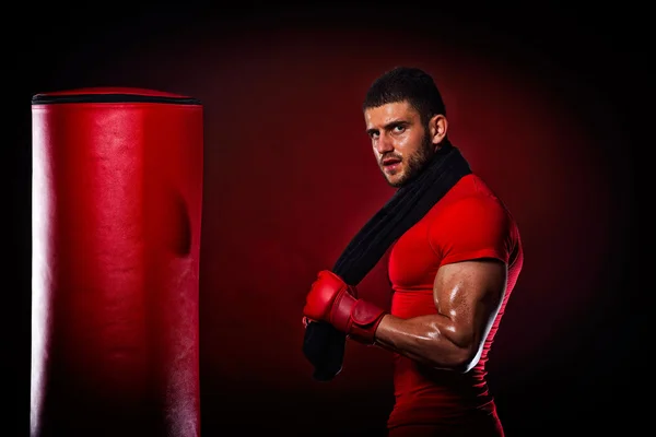 Jovem homem de pé por saco de boxe em estúdio — Fotografia de Stock