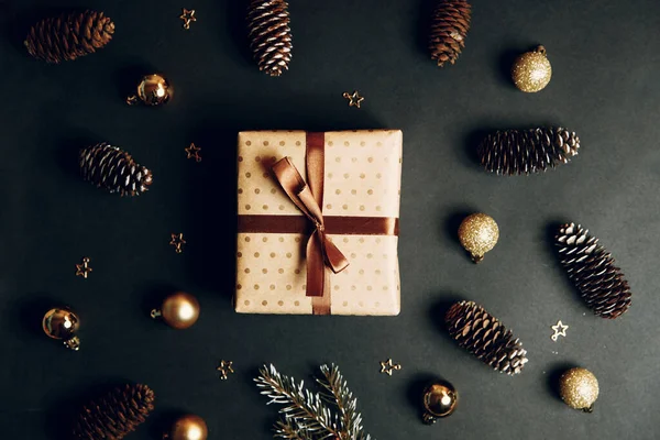 Kompozycja świąteczna z prezentem w pudełku. Złote zabawki, nowoczesne dekoracje wakacyjne, pudełka na prezenty, gałązki jodły na ciemnym czarnym tle. Elegancki szablon kartki świątecznej. — Zdjęcie stockowe