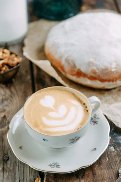 Breakfast with a buttered bun and a Cup of coffee. Cappuccino coffee on a wooden table with a loaf of bread.