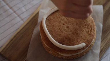 Kadın bir pasta şefi bisküvinin üzerine krema döker, hem de pasta poşeti ile, yakın çekim manzaralı. Bir pastane şefi ev yapımı Esterhazy keki hazırlar..