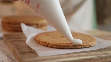 Kadın bir pasta şefi bisküvinin üzerine krema döker, hem de pasta poşeti ile, yakın çekim manzaralı. Bir pastane şefi ev yapımı Esterhazy keki hazırlar..