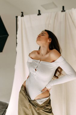 Basit giyinmiş güzel bir kızın kumaş üzerinde yapılan model testleri. Beyaz bir vücut giysisi içinde beyaz bir stüdyoda beyaz bir zeminde oturan ve penceresinden gölgeler süzülen sıska bir esmerin portresi..