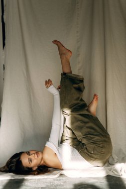 Basit giyinmiş güzel bir kızın kumaş üzerinde yapılan model testleri. Beyaz bir vücut giysisi içinde beyaz bir stüdyoda beyaz bir zeminde oturan ve penceresinden gölgeler süzülen sıska bir esmerin portresi..