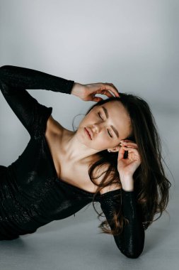 Beyaz siklonamada bir kızın model testleri. Siyah kısa elbiseli genç bir esmer poz verir ve yere yatar..