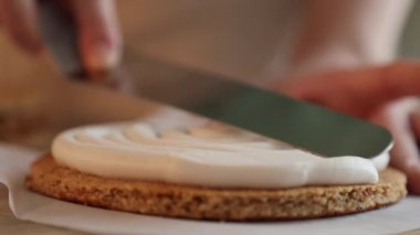 Kadın bir pasta şefi bisküvinin üzerine krema döker, hem de pasta poşeti ile, yakın çekim manzaralı. Bir pastane şefi ev yapımı Esterhazy keki hazırlar..