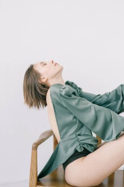 Parlak bir stüdyoda sandalyede oturan güzel bir kızın portresi. Işık arkaplanı üzerinde alışılmadık yakın çekim pozlarıyla model testleri.