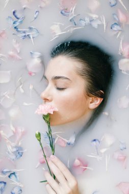 Spa tedavileri, yumuşak cilt ve yumuşak pastel gölgeler. Süt ve çiçeklerle dolu bir banyoda bir kadının şehvetli portresi..