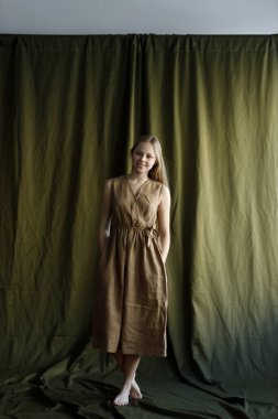 Stüdyoda bir bez parçasıyla deneme çekimi. Kumaş arka planda keten elbise içinde güzel bir genç kız..