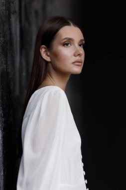 Genç, şık bir kadın, düğün modası, bahar trendi, siyah buket çiçek. Beyaz elbiseli gelin, şefkat, masumiyet, stüdyoda koyu bir arka plan..