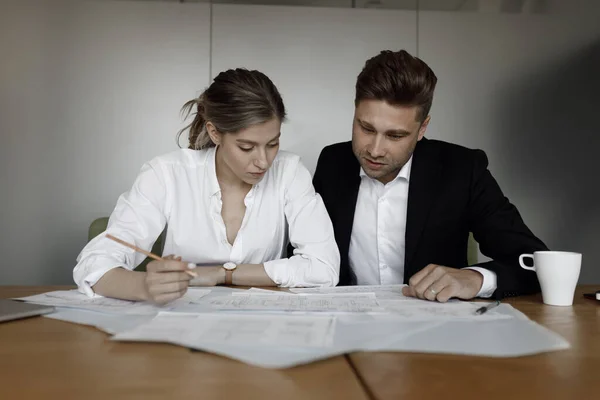 A man and a woman discuss business matters. A couple working at a laptop and blueprints in their home office smile.