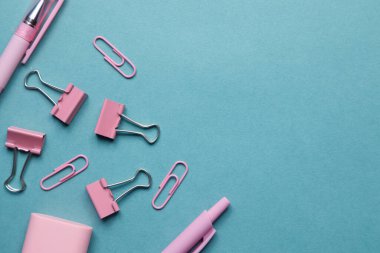 Boş mavi arkaplanı olan düz bir düzen. Okul teması üzerine düz bir kalem, ataç ve çıkartma..