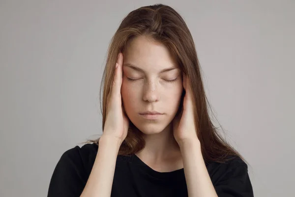 Una giovane donna con mal di testa, tenendo la testa, isolata su uno sfondo bianco. Ritratto di ragazza, tema medico, dolore ai templi. — Foto Stock
