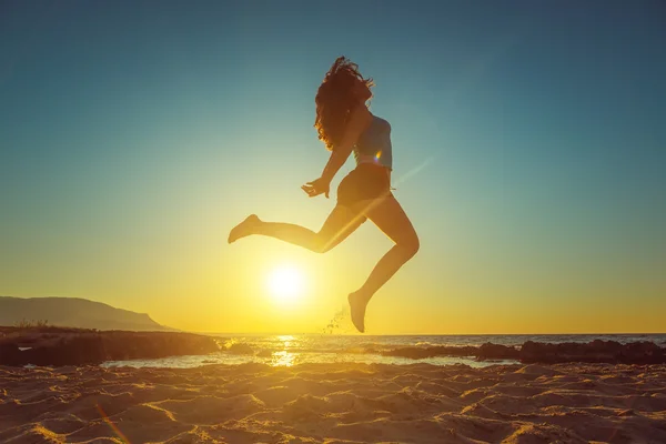 Fille heureuse sautant sur la plage contre le beau coucher de soleil — Photo