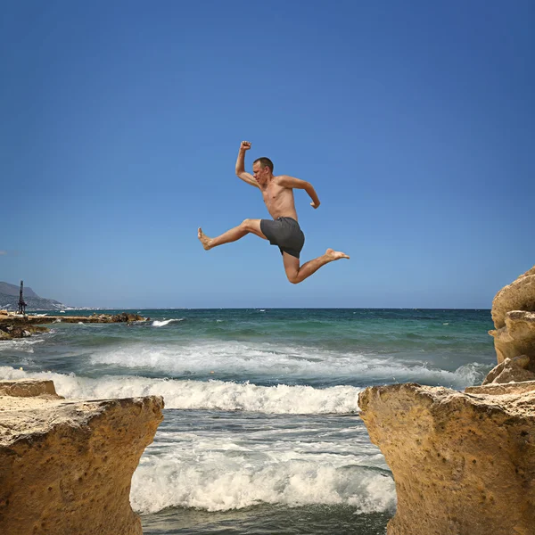 Man jumping over the abyss between two rocky mountains. — Stock Photo, Image
