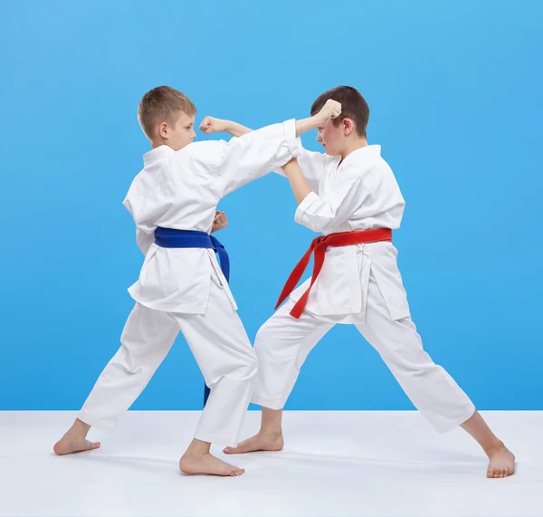 Chlapci jsou školení údery karate a bloky na modrém pozadí — Stock fotografie