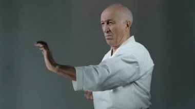 Beyaz bir karategi 'nin gri arka planında yaşlı bir sporcu elleriyle yumruk atıyor.