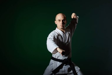 Karategi 'de, bir atlet fevkalade resmi karate egzersizlerini koyu yeşil arka planda yapar.