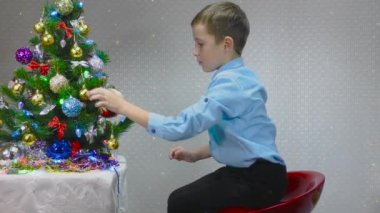 Mavi gömlekli çocuk yılbaşı oyuncaklarını Noel ağacında inceliyor.