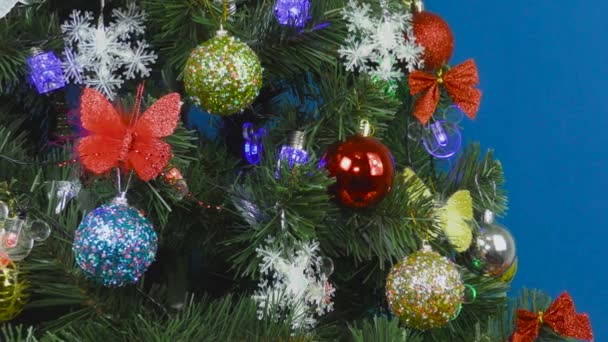 Голубом Фоне Рождественская Елка Украшена Разнообразными Красочными Игрушками — стоковое видео